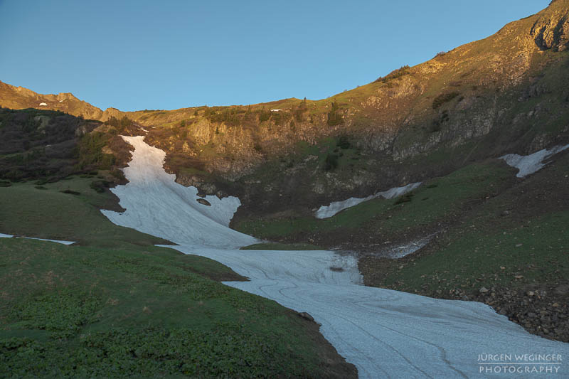 Schneefeld auf einem grünen Berghang, Sonnenaufgang