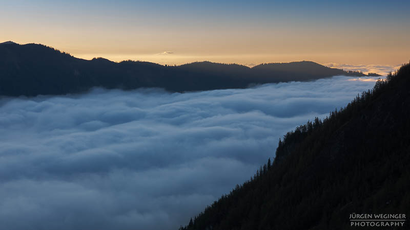 Nebeldecke über einem Tal mit Bergen im Hintergrund, Sonnenaufgang