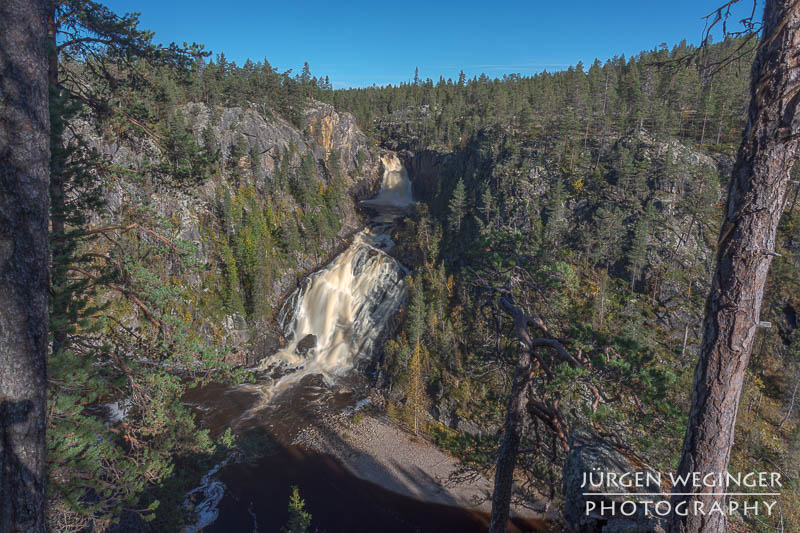 Ein Wasserfall in einer Schlucht umgeben von einem Wald und blauen Himmel im Muddus Nationalpark, Schweden